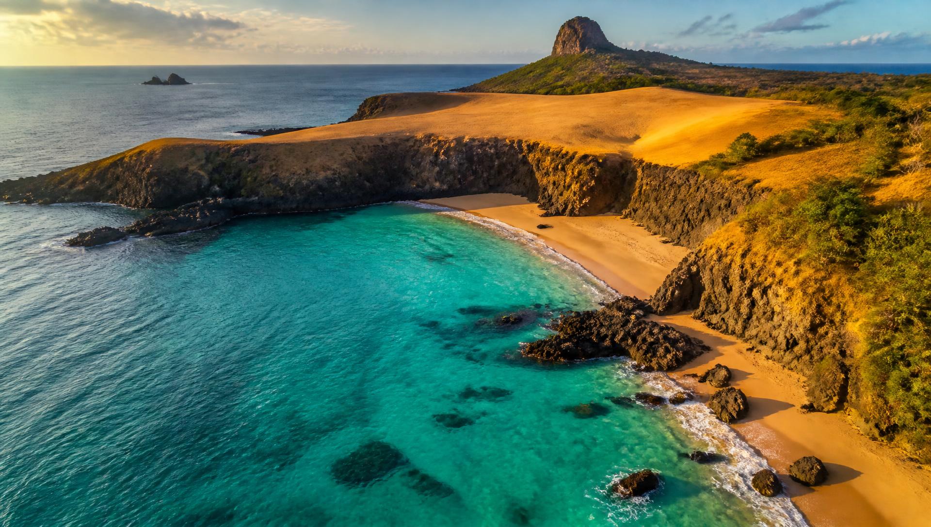Águas translúcidas de Fernando de Noronha encontrando dunas douradas ao pôr do sol
